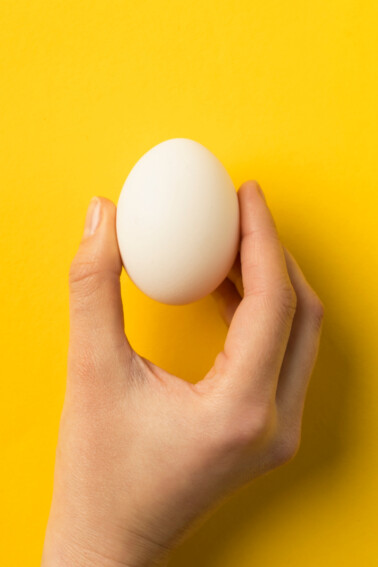Egg Shell Squeeze Kitchen Science Experiment for Kids - Kids Activities Blog - hand holding egg on yellow background