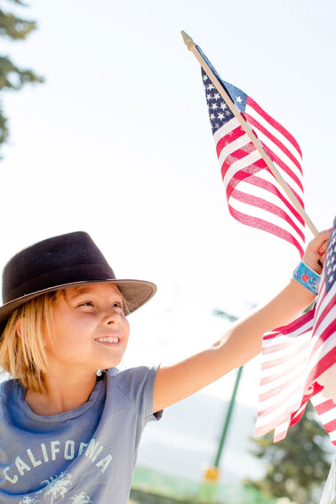 A young girl with a black hat on is holding an American flag in her left hand.