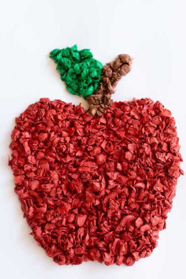 A piece of white cardstock with a red tissue paper apple on the front.