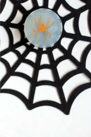 A black felt spiderweb with a bar of glycerin soap containing an orange spider inside.