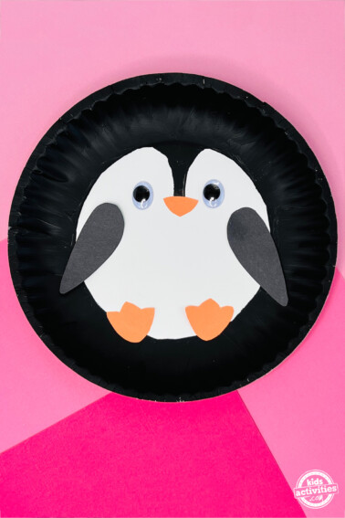 Paper plate penguin with googly eyes over a pink background. From Kids Activities Blog
