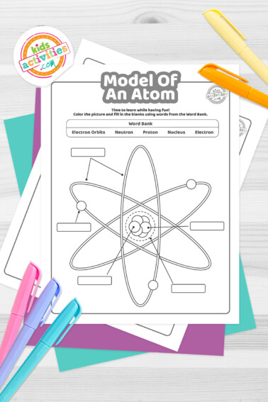 Black and white model of an atom coloring pages lying on top of a blue-green sheet with multicolored letters on a light gray background.